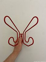 Front view of red wire wall hook held against a white background, showing the double hook design and mounting bracket.