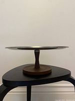 Side profile of circular stainless steel tray on walnut wood pedestal base, showing the overall shape and design.