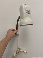 Front view of white articulating wall lamp held by hand showing power cord and switch.