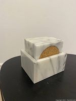 Set of square Carrera marble coasters stacked inside a marble holder on a black surface.