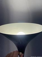 Close-up photo of lamp at lighted top with visible bulb under a white conical shade.