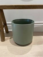 Green ceramic planter shown from side under wooden stool