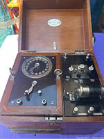 Full view of open wooden travel case with electrotherapy device showing circular dial, knobs, switches and coil.