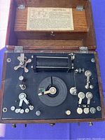 Top view of electrotherapy device control panel showing dials, levers, and central coil inside wooden case.