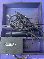 Open box showing black power box with company label, glass electrode attachments, and tangled cord connected to black handpiece inside lined box