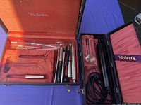 Open cases containing the main device, multiple glass electrodes, and metal attachments, all laid on red and purple fabric lining with visible wear.