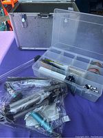 Photo of silver protective carrying case with combination lock and a plastic organizer box with compartments showing small camera accessory parts inside.