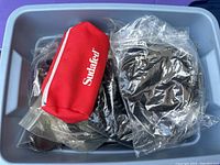 Top view of plastic bin with various black camera cords and a red Sudafed pouch sealed in bags.