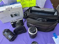 Full lot display including Olympus Pen PL1 camera with lens attached, two additional lenses, camera case, and original box.