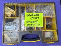 Top view of plastic storage box with transparent lid showing multiple compartments filled with various plastic and metal underwater camera accessory components, some bagged, some loose.