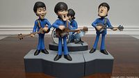 Front view of four Beatles figures with instruments on gray base