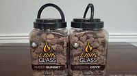 Two containers of Lava Glass flame dispersion rocks labeled Amber Sunset and Crystal Cove shown side by side on a table.