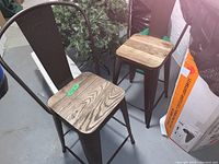 Three metal frame bar stools with wooden seats, black metal backrest and legs, natural wood seats with visible grain patterns.