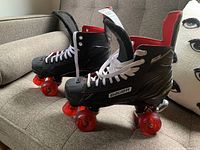Overall pair of black Bauer roller skates with red wheels, white laces, and red interior lining photographed on a beige couch.