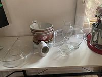 Set of seven Asian style ceramic bowls stacked with floral designs, five clear glass vases of various shapes, and three plates placed on a white table