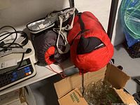 Two rolled, insulated Woods sleeping bags placed on shelving, red and gray colors visible with black carrying straps.