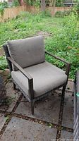 Front view of the outdoor chair showing the beige cushions and metal armrests with worn faux wicker sides.