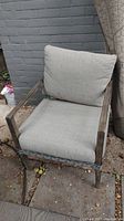 Front view of weathered gray faux wicker chair with thick light gray cushions, showing stains and outdoor setting.