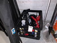 View of black crate filled with assorted aerosol cans, spray bottles, and a red brake caliper.