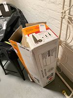 Box containing a 7 ft pre-lit pencil Christmas tree, located in a basement with other stored items.