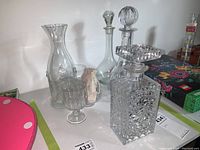 Four glass decanters arranged on a surface with three different glasses, showing variety in shapes and styles including one cut crystal decanter.