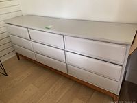 Front perspective of the white painted wood dresser showing nine drawers in three rows of three.