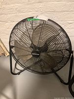 Side angled view showing the full metal protective grill, blades, and stand of the fan in a basement setting.