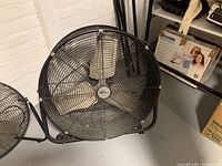 Front view of large black industrial drum fan showing three metal blades and protective grill.