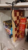 Photo showing stacked puzzles, wooden chess board, and Melissa & Doug Suspend game container under a shelf.