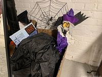 Photo of deflated Halloween inflatable including spider web and character inside a cardboard box against a brick wall.