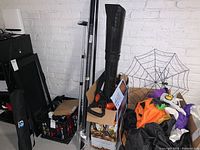 Leaf blower standing in box with some poles and other items nearby on floor against a white brick wall in basement.