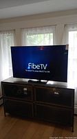 Front view of TV powered on displaying FibeTV prompt, sitting on wooden console with mesh-front cabinets.