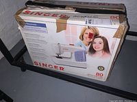 Original packaging for Singer electronic sewing machine showing brand, model 7422, and key features like 80 stitch functions