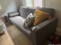 Front angle view of grey tufted sleeper sofa bed with accent pillows