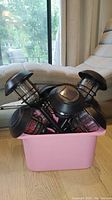 Eight black solar garden lights inside a pink rectangular plastic bin, showing solar panels and light housings.