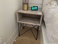Side table placed beside bed on wooden floor showing wood grain top and black metal legs, small decorative items on top.
