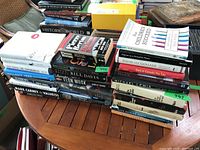 Photo of multiple stacks of various non-fiction hardcover and softcover books on a wooden table.