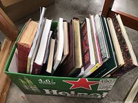 Top view of the box showing a variety of books with different sizes and covers inside a Heineken beer box.