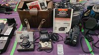 Full overview of all lot items including Pentax ME Super with lens, Pentax Espio 105G, JVC GR-AX7 camcorder, instruction manuals, carrying cases, and cables