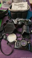 Photo showing Nikon F50 camera with Tamron zoom lens attached, Nikon 50mm f/1.8 lens on film camera body, carrying cases and manuals.