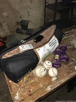 Photo of the croquet set in a black carry bag, three baseballs, two purple dumbbells on a wooden surface in basement.