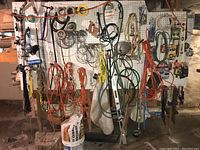 Wide shot of wall-mounted pegboard with numerous hanging extension cords, wires, chains, hardware, and paint brushes.