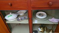 Image showing plates, serving dishes, and decorative brass items inside a wooden cabinet with two drawers and glass doors.