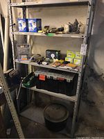 Full view of shelving unit contents including floodlight bulbs, wire brushes, chisels, power sander, mask, black toolbox, large pot, and other tools