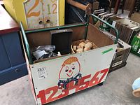 Side view of metal toy box on casters showing numbered print and a cartoon character on front