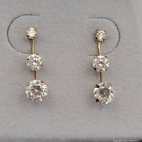 Close-up image of gold earrings showing three graduated cubic zirconia gemstones on each earring, set vertically.