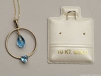 Close-up of the gold pendant with two blue topaz stones alongside original 10kt gold packaging.