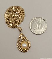 Necklace coiled with teardrop pearl pendant beside a Canadian dime for scale