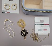 Top down photo showing the earrings on original card, two necklace chains including one with the black enamel flower pendant, and the two-tone bracelet along with the blue velvet storage box opened.