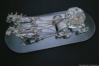 Crystal horse-drawn carriage figurine with two horses and an oval glass base. The horses have flowing manes and are connected with silver chains as reins to the faceted carriage.